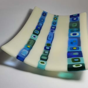 May include: A white glass serving dish with three vertical stripes of blue, green, and yellow geometric shapes.