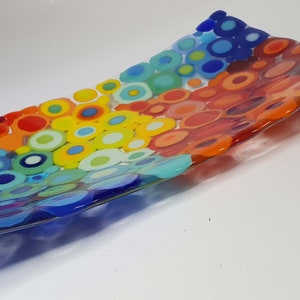 Puede incluir: Un plato de servir rectangular de vidrio con un diseño colorido de círculos superpuestos en tonos de rojo, naranja, amarillo, verde, azul y morado.