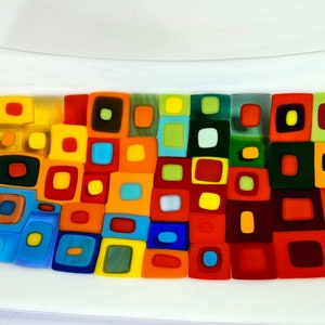 Puede incluir: Una bandeja rectangular de servir de vidrio con fondo blanco y un diseño de mosaico colorido. El mosaico está formado por pequeños cuadrados en varios tonos de rojo, naranja, amarillo, verde, azul y negro.