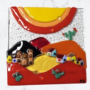 Puede incluir: Una obra de arte de mosaico de vidrio colorido que representa un paisaje desértico con un sol amarillo, colinas rojas y pequeñas casas. La obra de arte presenta un cactus y las iniciales "CS" en la esquina inferior derecha.