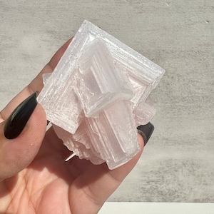 May include: A large, pink Himalayan salt crystal with a geometric shape. The crystal is translucent and has a natural, rough texture.