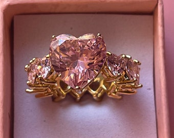 May include: A gold ring with a large pink heart-shaped gemstone surrounded by smaller clear gemstones.
