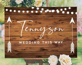 May include: Rustic wooden wedding sign with white text that reads "Tennyson Wedding This Way" with white arrows on either side. The sign is decorated with a string of white lights.