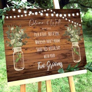 May include: Rustic wooden wedding sign with white text that reads "Oliver & Will 09-03-2022 Pick a seat, not a side Wherever there's room Share this special day with your Two Grooms". The sign is decorated with greenery and mason jars.