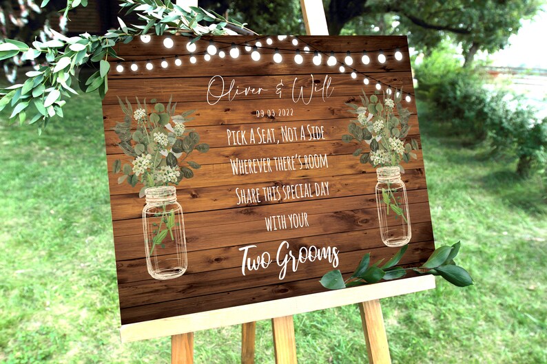 May include: Rustic wooden wedding sign with white text that reads "Oliver & Will 09-03-2022 Pick a seat, not a side Wherever there's room Share this special day with your Two Grooms". The sign is decorated with greenery and mason jars.