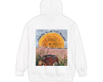May include: A white hoodie featuring a graphic print on the back. The design shows a large yellow sun rising over a field of pink flowers and a vintage red car. The text "JOIN THE SLOW FOOT MOVEMENT" is arched over the sun in black lettering.