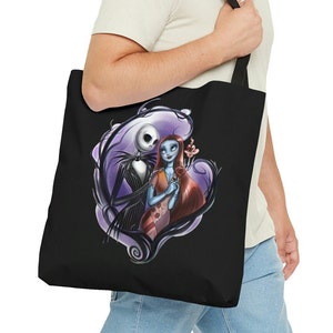 Pode incluir: Uma bolsa tote preta com um gráfico de Jack Skellington e Sally de O Estranho Mundo de Jack. O gráfico mostra eles se abraçando com um fundo roxo e preto.