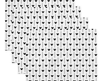 May include: A set of four rectangular placemats featuring a repeating pattern of black Mickey Mouse silhouettes and vertical columns of small black chevron arrows arranged on a crisp white background, creating a clean and uniform graphic design.