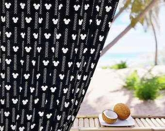 May include: Black curtain with a white Mickey Mouse head pattern and arrow design. The curtain is partially drawn, revealing a tropical beach scene with palm trees and the ocean. Two coconuts sit on a bamboo table.