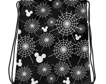 May include: A black drawstring backpack featuring a repeating pattern of white spider webs and white mouse-ear silhouettes. The bag has black cord straps that cinch the top closed, creating a gathered opening at the top of the rectangular bag.