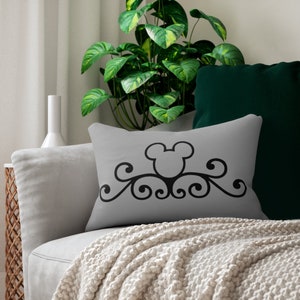 Puede incluir: Una almohada gris con una silueta negra de la cabeza de Mickey Mouse y un diseño decorativo de desplazamiento.