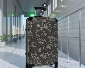 May include: A dark gray rolling suitcase featuring a white outline pattern of Mickey Mouse. The suitcase has a retractable handle and four wheels. The luggage is in a hallway with a tiled floor and a metal railing.