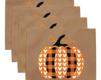 May include: A set of four rectangular tan placemats, each featuring a central pumpkin graphic. The pumpkin has alternating vertical segments of orange with white mouse-ear silhouettes and black and orange buffalo plaid patterns.