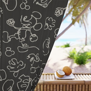 May include: A black sheer curtain with a white abstract pattern hangs in front of a tropical beach scene. Two halves of a coconut are on a white plate on a bamboo table.