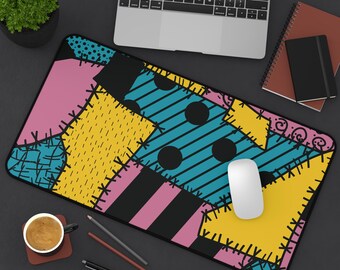 May include: A rectangular mousepad with a patchwork design in pink, yellow, teal, and black. The design includes stripes, dots, and stitched patterns. A white mouse sits on the pad, with a laptop and other office supplies in the background.
