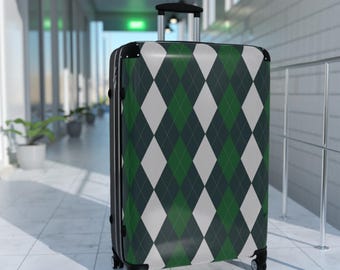 May include: A rolling suitcase with a green, white, and dark green argyle pattern. The suitcase has a retractable handle and four black wheels. The luggage is in a hallway with white tile flooring and potted plants.