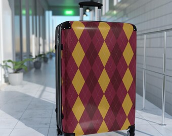 May include: A rolling suitcase with a burgundy and gold diamond pattern. The suitcase has a black frame, a retractable handle, and four wheels. The luggage is in a hallway with white tile flooring and potted plants.