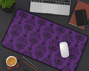 May include: A rectangular desk mat featuring a vibrant purple background with a repeating black damask-style pattern. The mat has rounded corners and a black stitched border, providing a smooth surface for computer mouse and keyboard use.