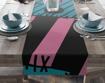 May include: A rectangular table runner featuring a patchwork design with alternating panels of black, dusty pink, and light blue. The pattern includes dark gray diagonal stripes and black stitched cross-hatch details across the fabric surface.