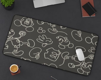 May include: A black mouse pad with a white outline of Mickey Mouse and other Disney characters. The mouse pad is on a black surface with a laptop, a cup of coffee, and pencils.