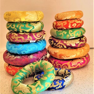 以下が含まれることがあります： 複雑な金の模様が施されたカラフルな瞑想クッションの積み重ね。クッションはネパール製で、瞑想やヨガの際に座るのに最適です。