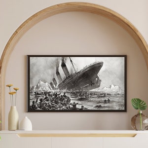 May include: A black and white photograph of the RMS Titanic sinking. The ship is partially submerged in the water, with people in lifeboats and on deck. The image is framed and displayed on a white shelf above a white cabinet.