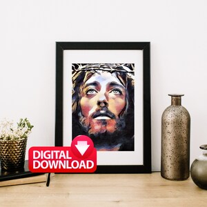 May include: A digital download of a painting depicting a man with a crown of thorns, looking up with a sorrowful expression. The painting is in a black frame and is displayed on a table with other decorative items.