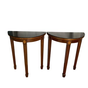 May include: A pair of half-moon tables with dark tops and brown wooden legs. The tables feature a classic design with decorative accents, suitable for a living room or hallway. Each table is approximately 76 cm in height.