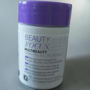 Peut inclure: Une bouteille de supplément blanche avec un couvercle violet. L'étiquette indique "BEAUTY FOCUS. MULTIBEAUTY FOR BEAUTIFUL SKIN, HAIR, AND NAILS." La bouteille contient 30 gélules. Complément alimentaire.