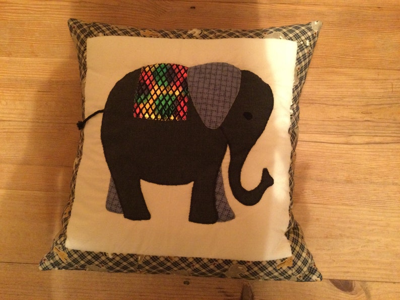 Peut inclure: Un oreiller blanc avec une applique d'&eacute;l&eacute;phant noir et bleu. L'&eacute;l&eacute;phant a une selle &agrave; motifs color&eacute;s.