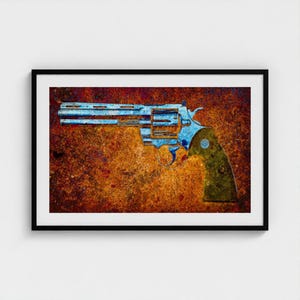 May include: A framed wall art print featuring a blue-toned revolver silhouette set against a highly textured, deep orange and rust-colored background. The firearm is depicted in profile, showcasing the barrel, cylinder, and grip in a stylized manner.