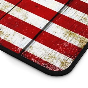 Puede incluir: Una bandera estadounidense roja, blanca y azul impresa en una superficie de madera. La bandera est&aacute; desgastada y descolorida, lo que le da un aspecto vintage.