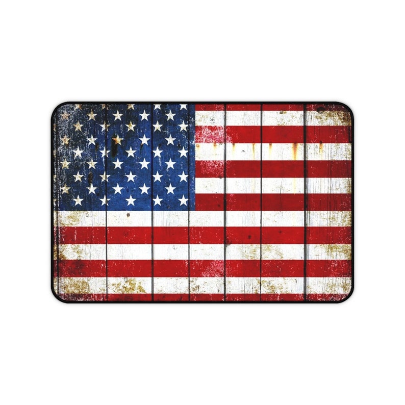 Puede incluir: Un letrero de madera desgastado con un dise&ntilde;o de bandera estadounidense descolorido. La bandera es roja, blanca y azul con estrellas blancas sobre un campo azul. El letrero tiene un borde negro.