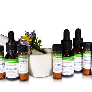 May include: A collection of ten small glass bottles with dropper tops, filled with orange and white pellets. The bottles are labeled with the words "Smarthealth Naturopathics" and various ailments, including "Ear Infection", "Acne", "Staph", "Feline-Vomit", "Feline Kidney", "Carpal Tunnel", and "PMS".