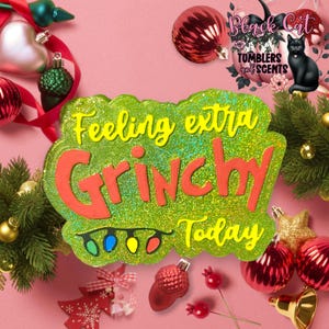 May include: Green glitter sign with the text "Feeling extra Grinchy Today" in red and yellow letters. The sign has a string of colorful lights at the bottom.