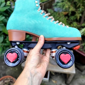 May include: Teal suede roller skates with black and red wheels. The wheels have a heart-shaped design.