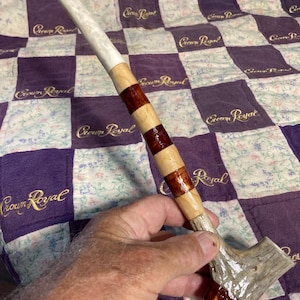 May include: A handcrafted pipe featuring a long, cylindrical stem made of alternating segments of light-colored wood and polished dark reddish-brown wood, topped with a smooth white mouthpiece and a textured, natural-looking antler bowl base.