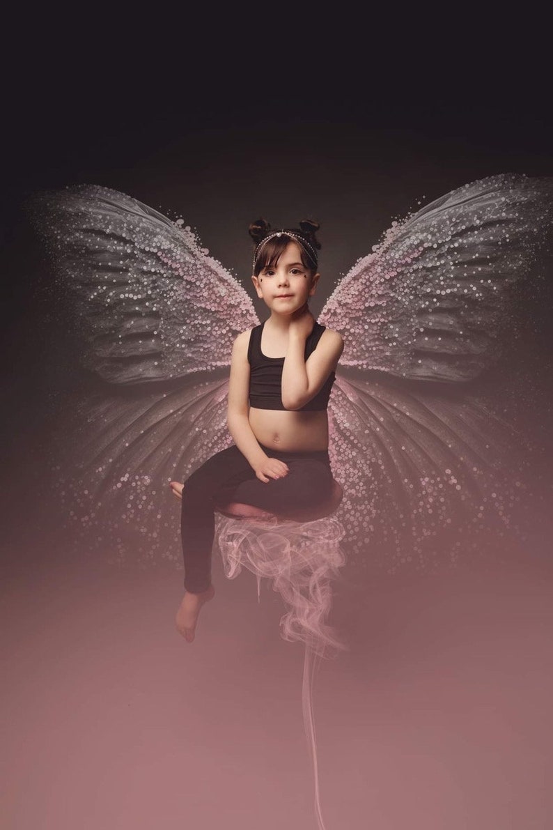 Puede incluir: Una persona joven con un top negro sin mangas y leggings negros se sienta en una nube con grandes alas de mariposa rosadas detr&aacute;s de ella.