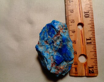 Może przedstawiać: Żywy niebieski okaz minerału o szorstkiej, teksturowanej powierzchni. Skała ma około 7,6 cm długości, z drewnianą linijką jako skalą. Minerał wykazuje mieszankę głębokich i jasnych odcieni niebieskiego z nutami czerwonobrązowego.