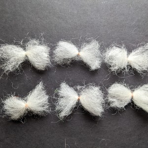 May include: Eight white fluffy bows tied with a thin copper wire. The bows are arranged in two rows of four on a dark gray surface.