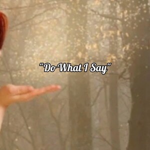 Puede incluir: Una mano de mujer extendida en un entorno de bosque con un fondo borroso. El texto "Do What I Say" está superpuesto a la imagen.