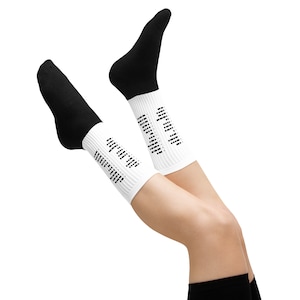May include: A pair of black and white socks. The socks have black tops and white ribbed cuffs. The cuffs feature a repeating black dot pattern. The socks are shown against a white background.