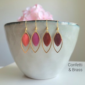 Könnte beinhalten: Vier Paar goldene Ohrringe mit einem tropfenförmigen Design. Jeder Ohrring hat eine doppelte Goldschicht mit einem farbigen Harzeinsatz. Die Farben der Harzeinsätze sind Koralle, Rosa, Burgunder und Rotbraun.