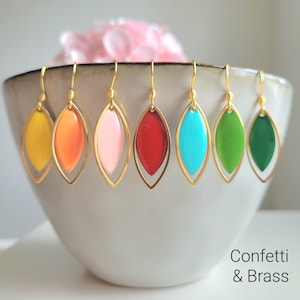 Könnte beinhalten: Ohrringe in Tropfenform in den Farben Gelb, Orange, Rosa, Rot, Türkis, Grün und Dunkelgrün. Jeder Ohrring hat einen goldfarbenen Rahmen und eine glänzende Emaille-Oberfläche. Der Text "Confetti & Brass" ist sichtbar.