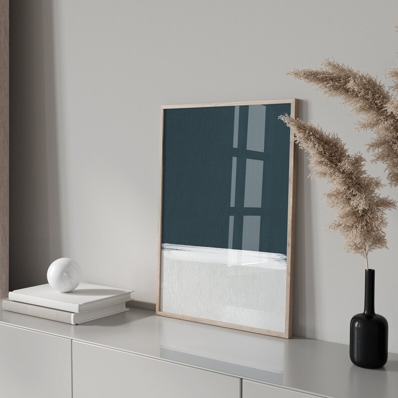 May include: A framed abstract painting with a teal blue background and a white horizontal line. The painting is hanging on a white wall above a light grey cabinet.