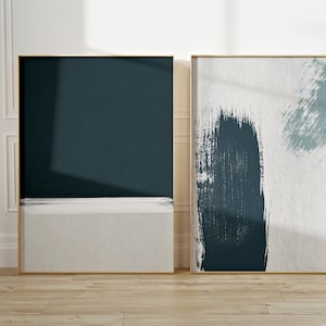 May include: Two framed abstract art prints with a teal and white color scheme. The print on the left is a solid teal color with a thin white stripe across the bottom. The print on the right has a white background with teal brushstrokes.