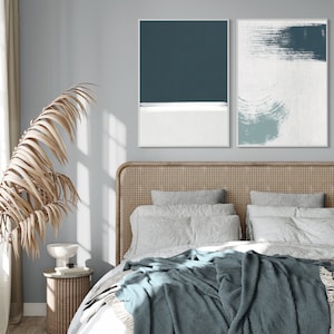 May include: A bedroom with a bed featuring a woven headboard, white bedding, and a blue throw blanket. Two abstract paintings in blue and white tones hang above the bed.