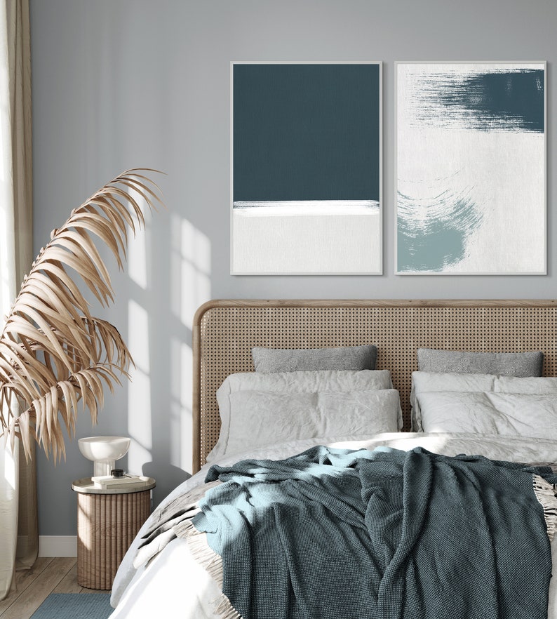 May include: A bedroom with a bed featuring a woven headboard, white bedding, and a blue throw blanket. Two abstract paintings in blue and white tones hang above the bed.