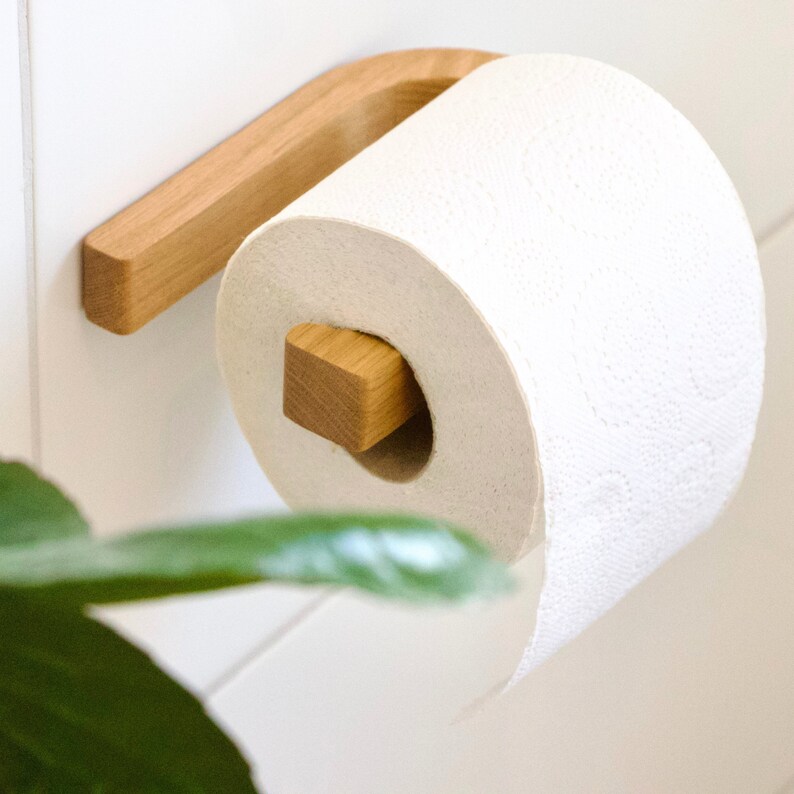 May include: A wooden toilet paper holder with a roll of white toilet paper. The holder is mounted to a white wall.
