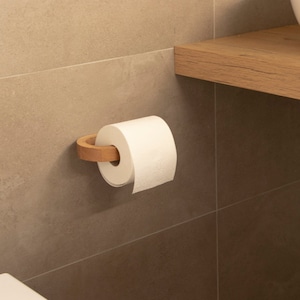 May include: A white toilet paper roll on a wooden toilet paper holder mounted on a beige tiled wall.